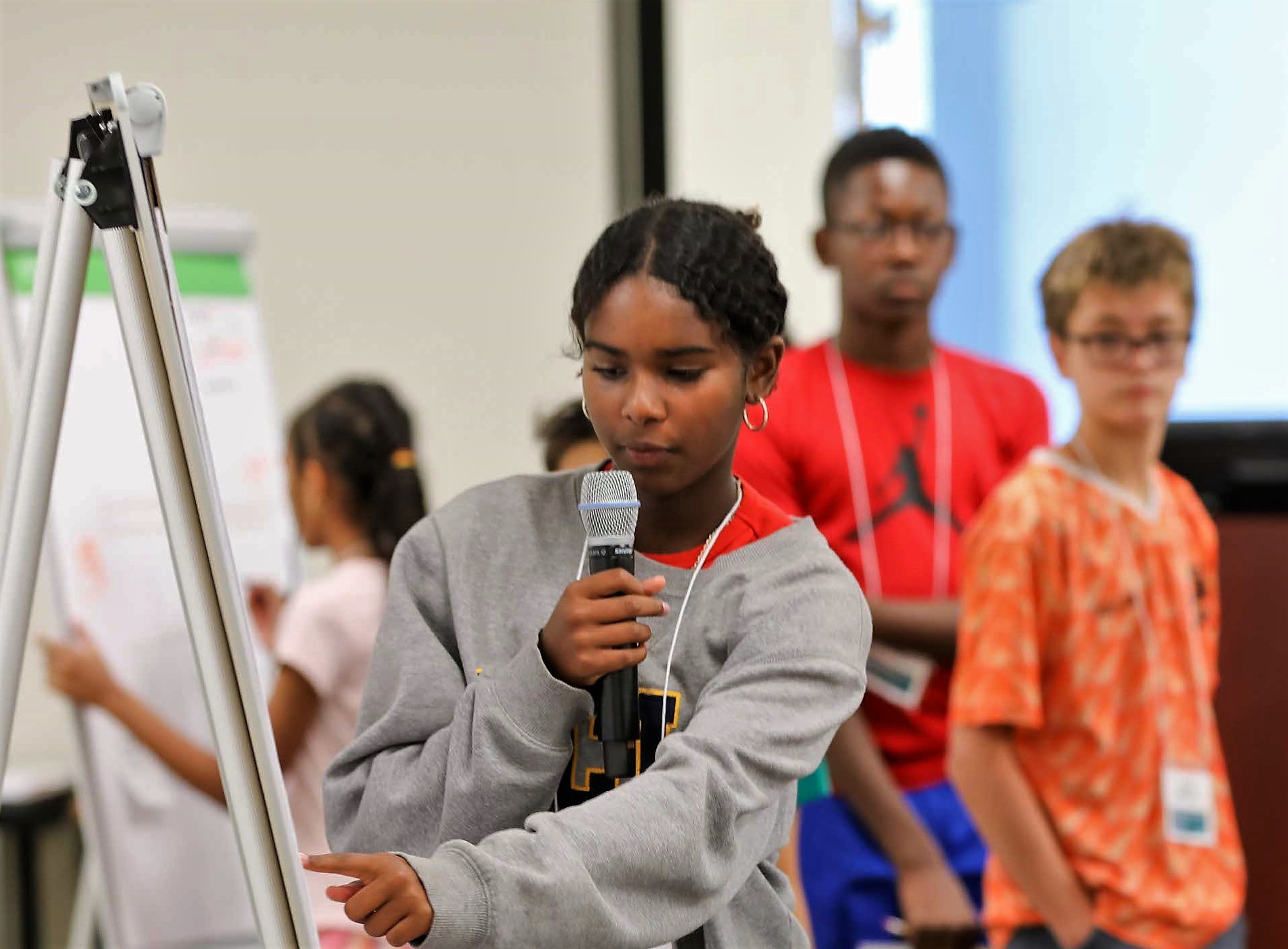 Camper holding microphone pointing at presentation on easel