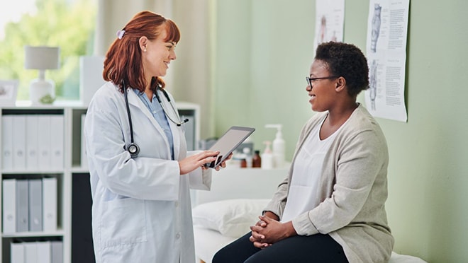 Doctor standing and talking to her patient who is sitting on the exam table