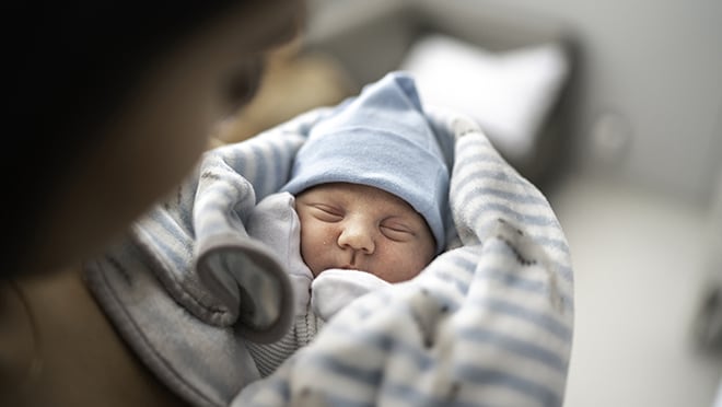 A person holds a sleeping, comfortably swaddled infant.