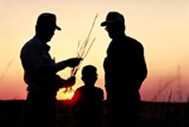 photo of a sunset with three generations og males standing in it.