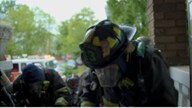 Shows a firefighter in full gear at a row house fire.