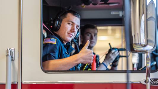 Close-up of two emergency responders inside of an emergency vehicle. One of the emrgency responders is giving the thumbs-up hand signal. Comradery concept