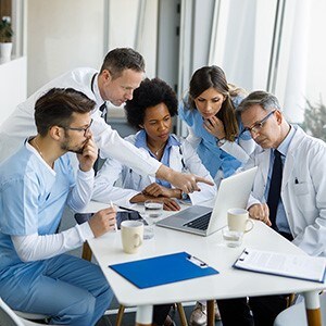 Physicians and nurses meeting and discussing item on laptop.