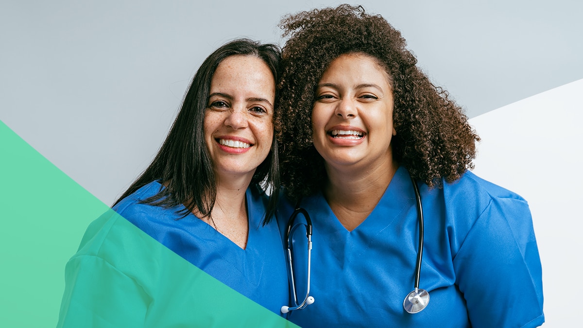 Two healthcare workers pose together with big smiles.