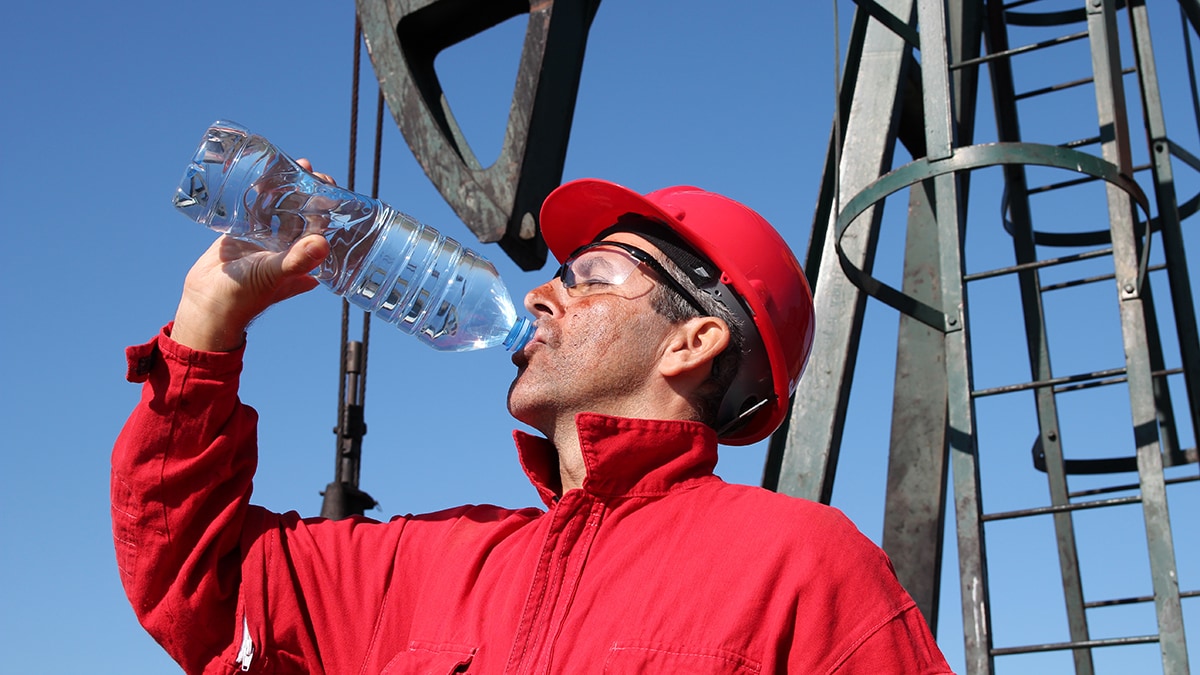 Construction worker wearing a red jacket and red hard hat drinking water