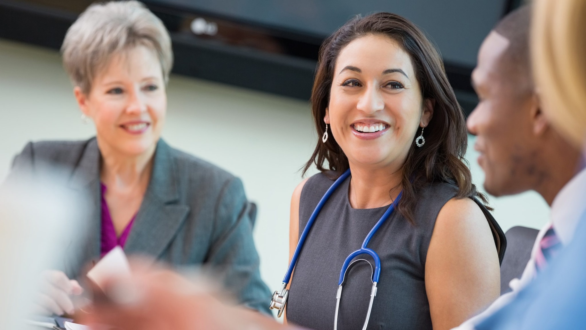 woman wearing stethoscope around her neck sitting around a table with other people