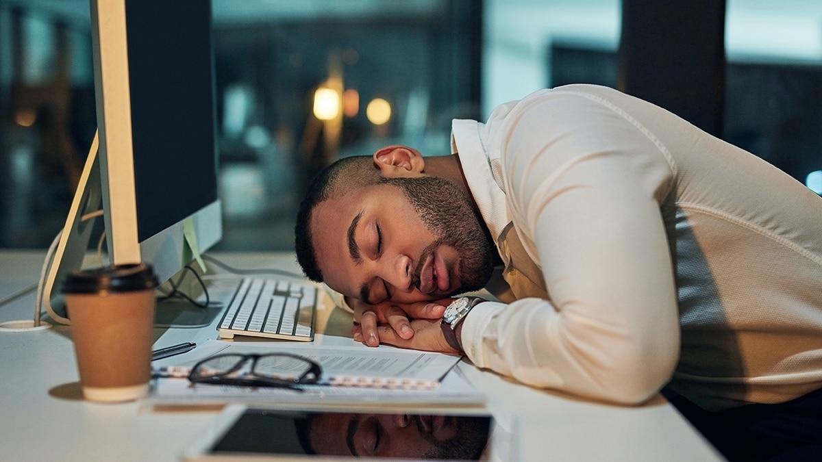 Exhausted African American businessman wearing a tan colored shirt is sleeping at his desk during a late night at work.