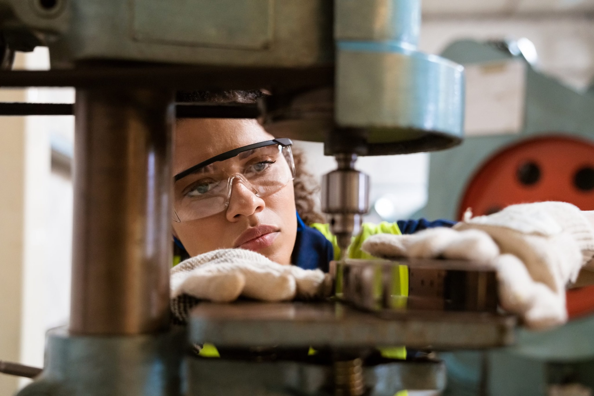 Close up of a young female manufacturing worker wearing safety glasses and gloves using a machine.