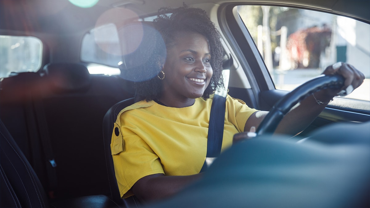 Young black female driver in yellow shirt driving a car and focusing on the road.