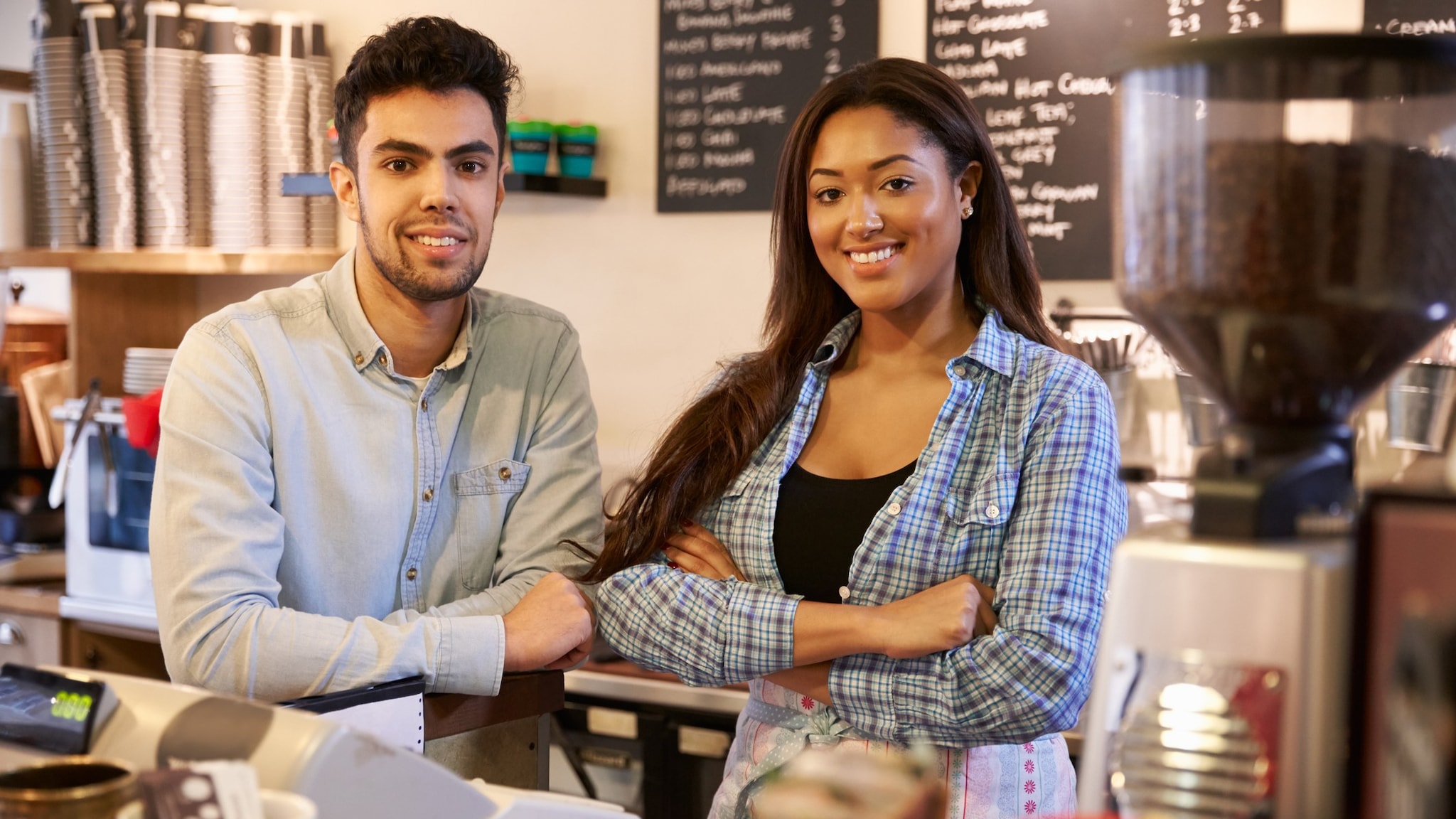 Trabajador y trabajadora jóvenes parados detrás del mesón de una cafetería.