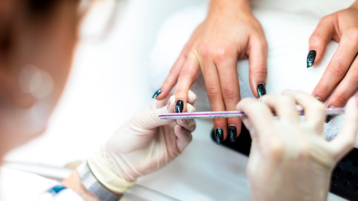 Nail technician wearing gloves, working with someone's fingernails.