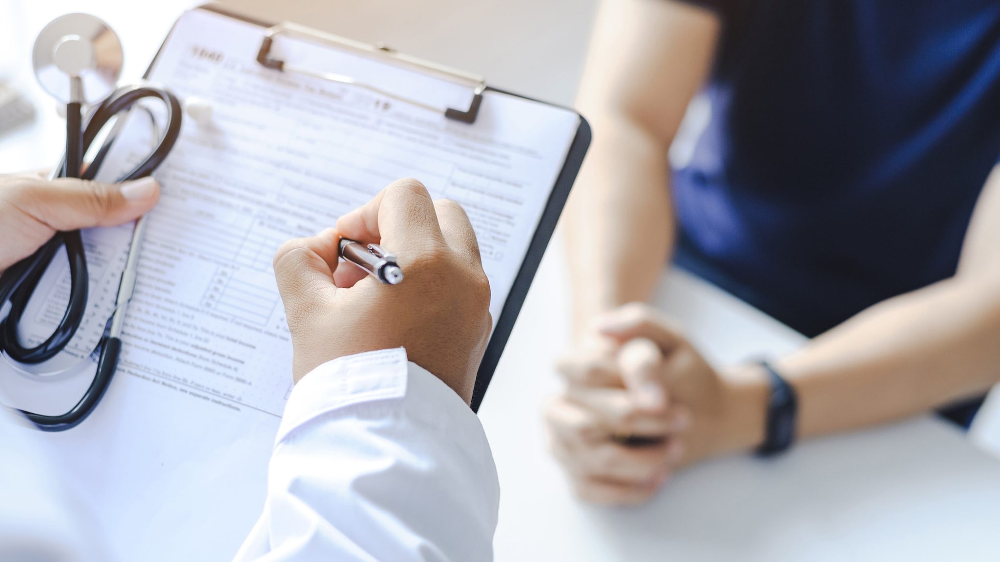 Doctor giving prescription to the patient and filling up medical form at a clipboard.