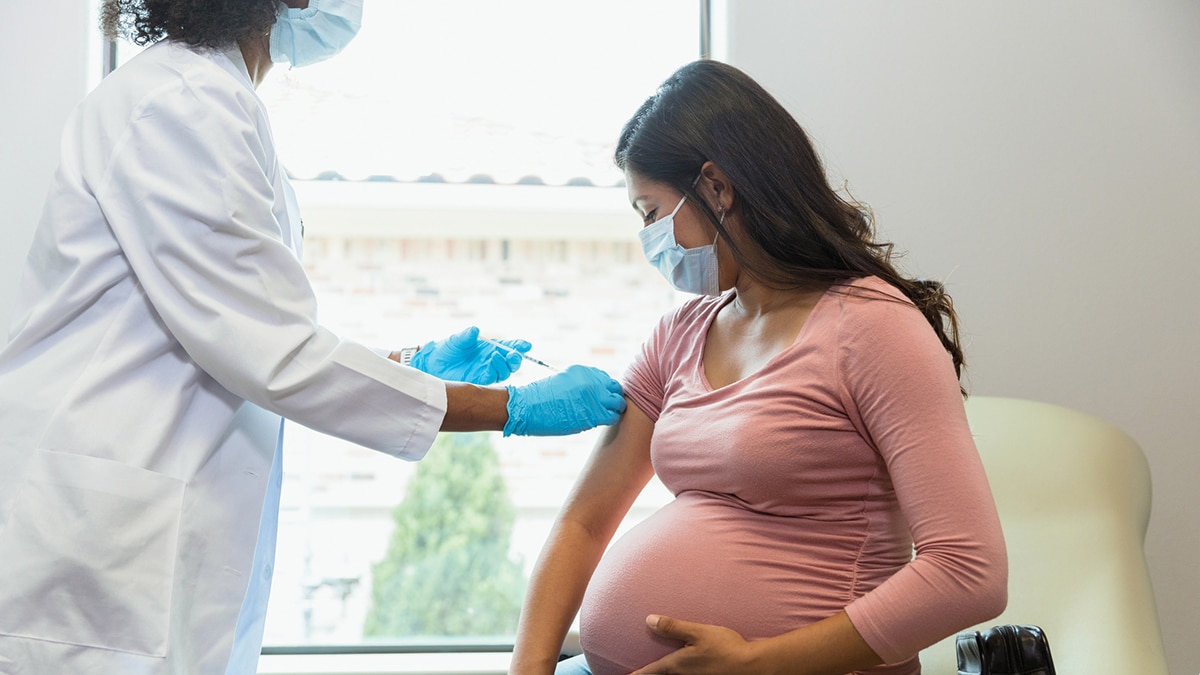 Proveedora de atención médica trabajando con una paciente embarazada, ambas usando EPP.