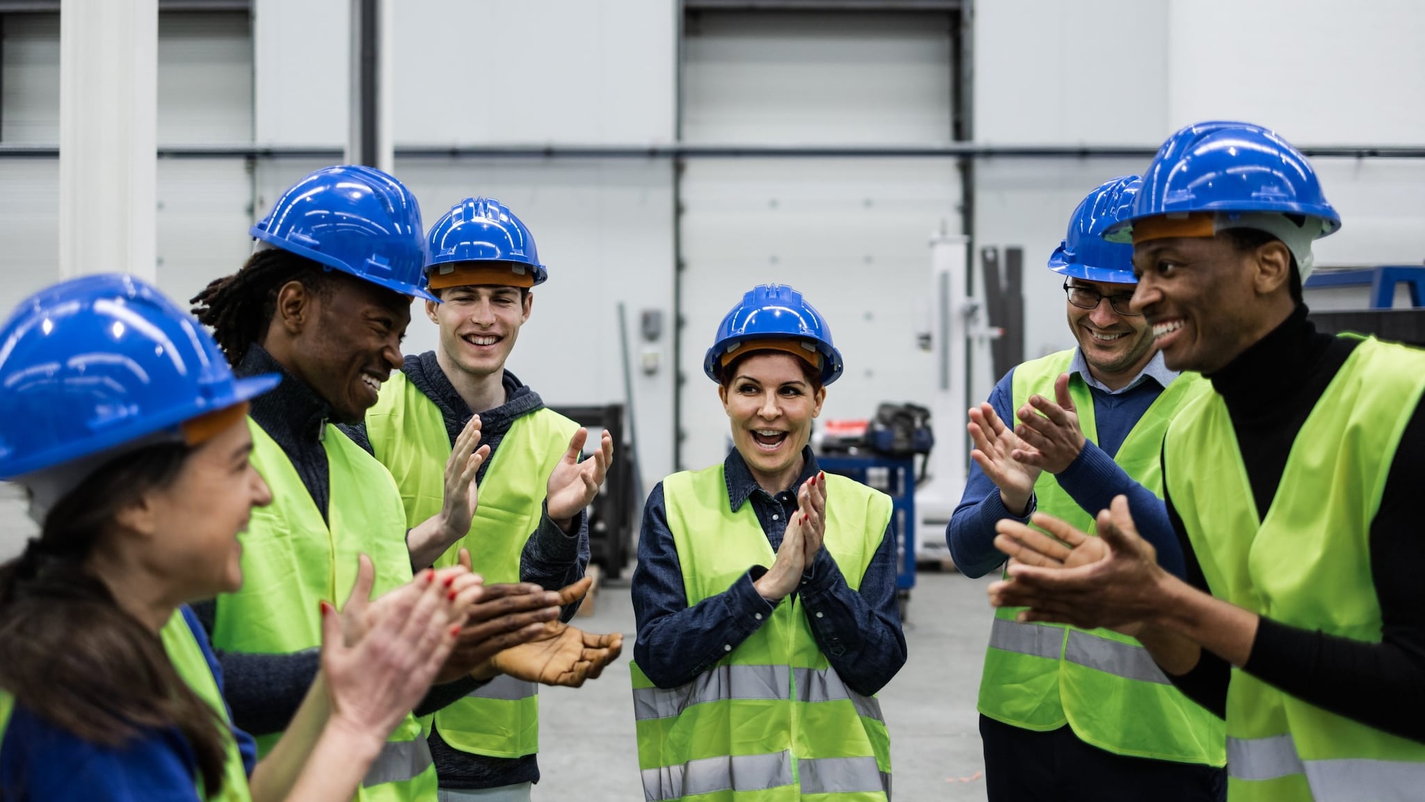 A group of young adults standing in a half circle in safety vests and hardhats.