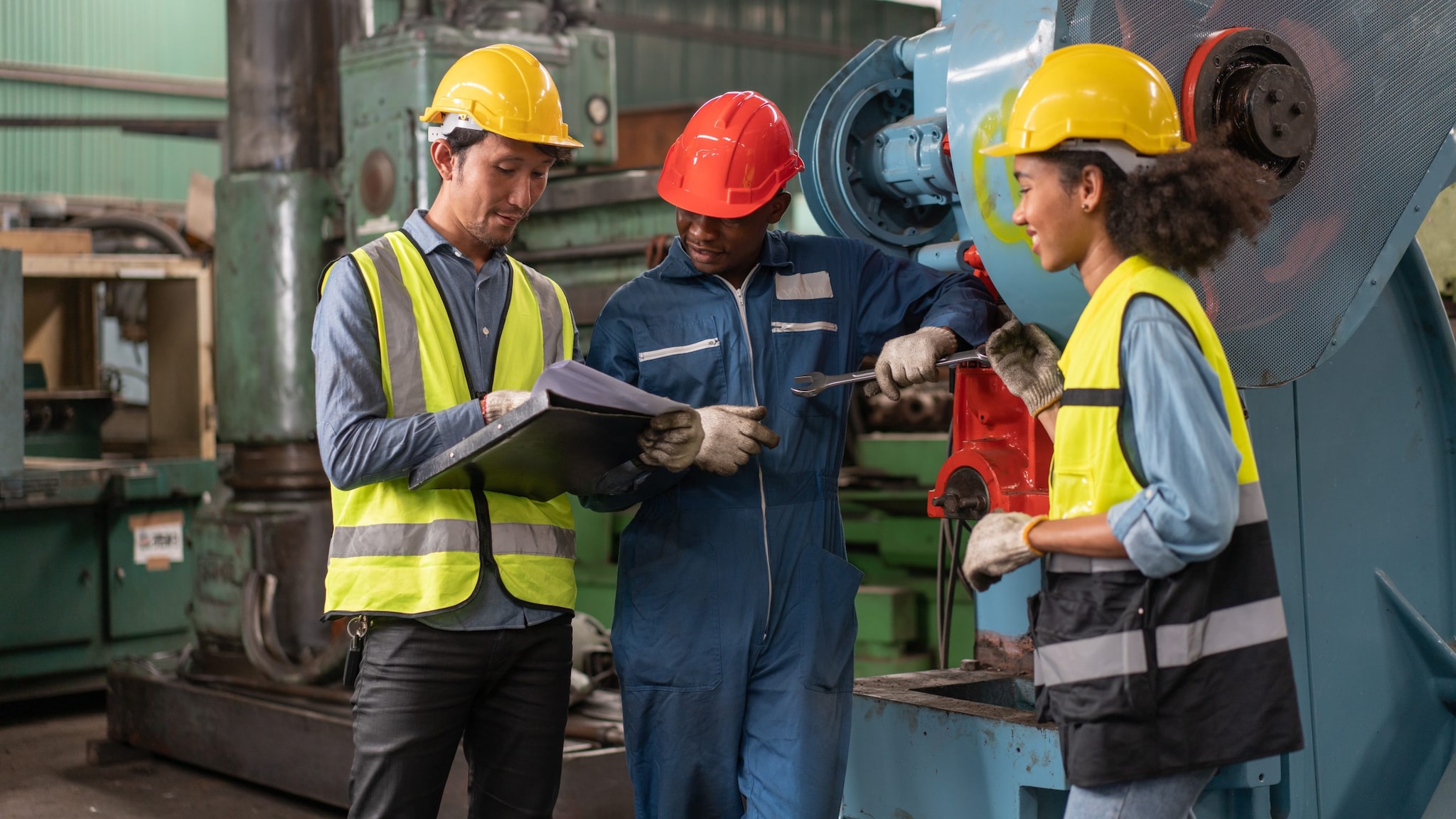 Engineers in safety vest with helmet in front of a factory machine.