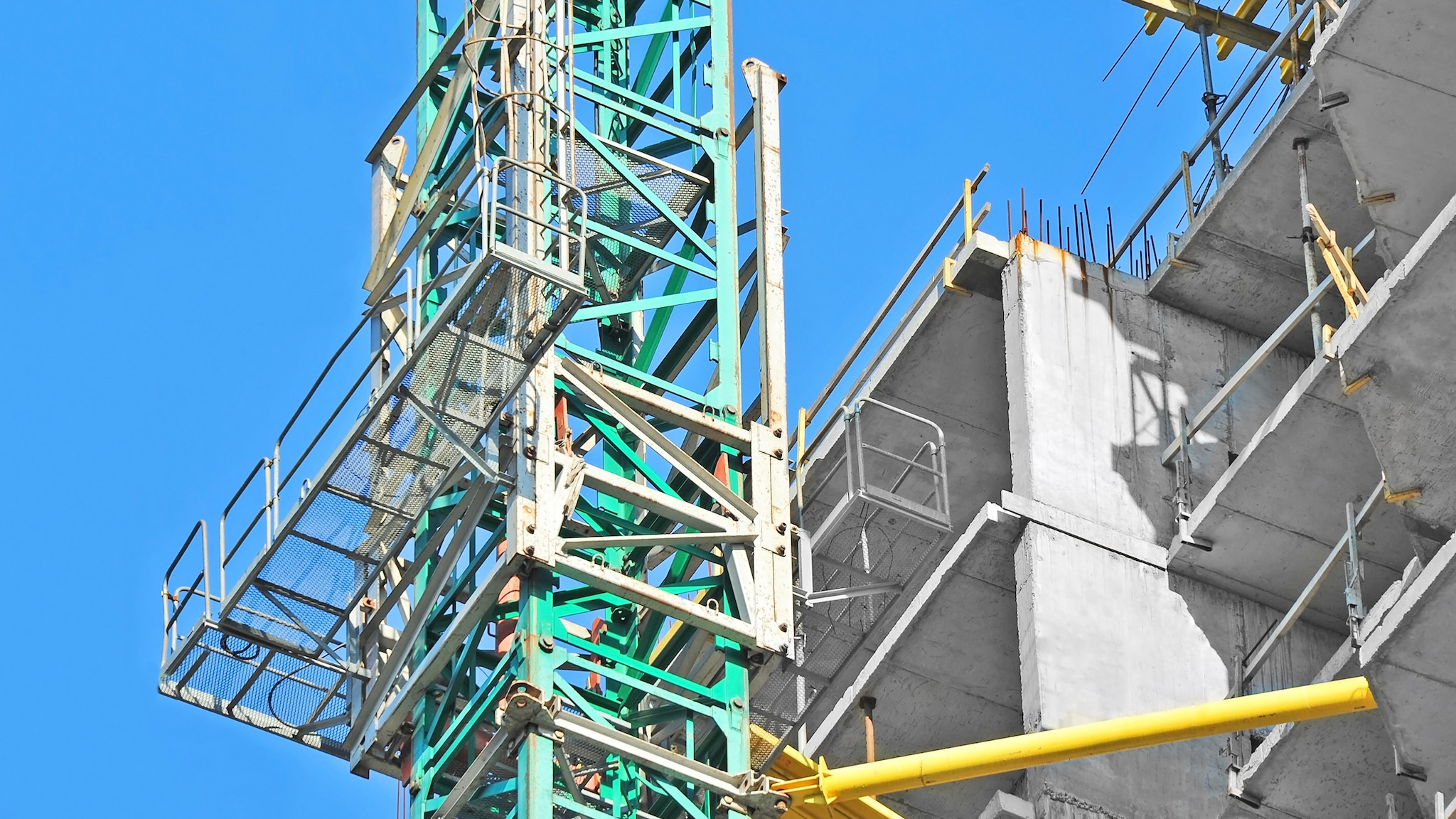 Plataforma elevadora sobre mástil al lado de una edificación en construcción.