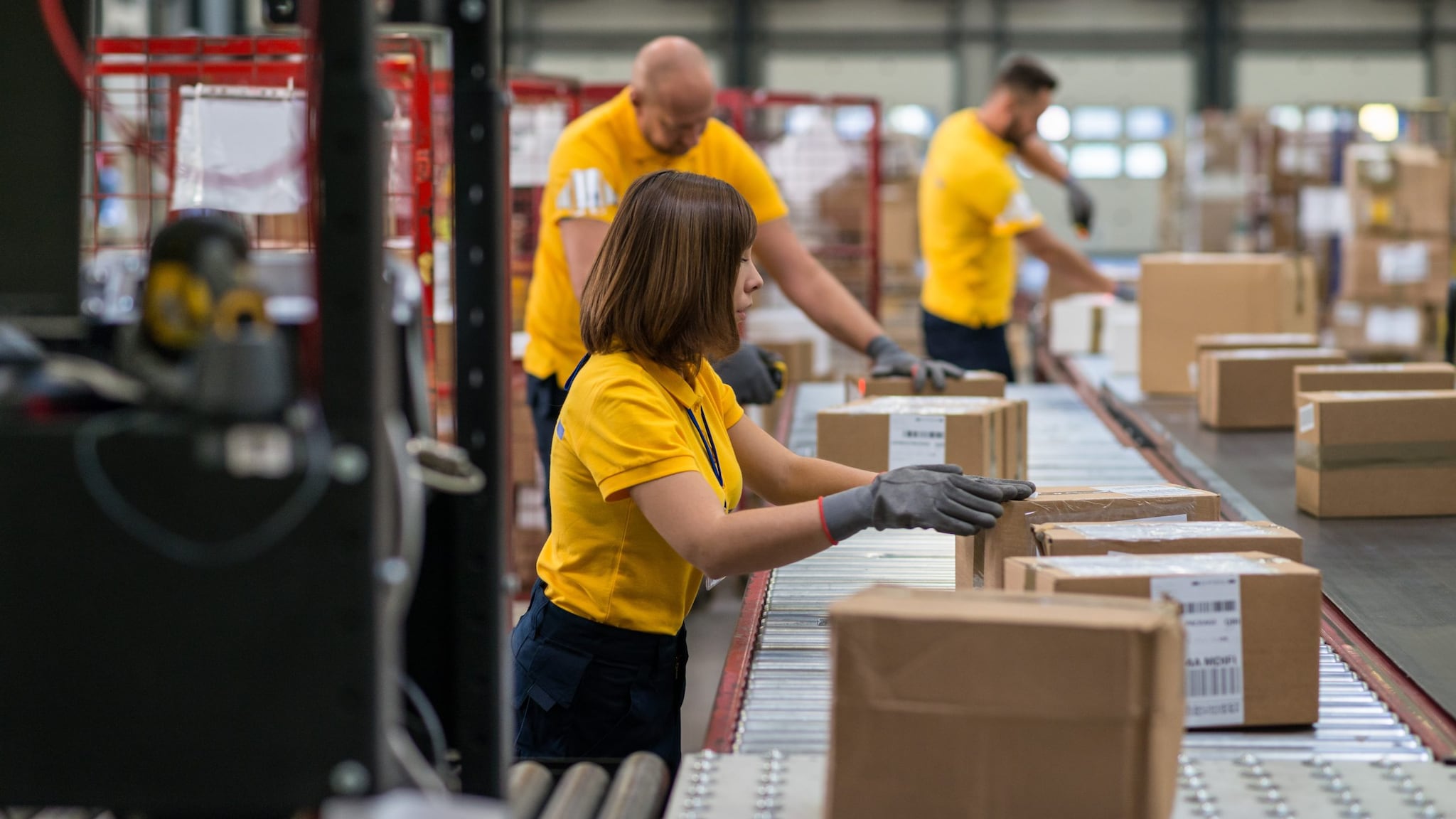 Trabajadores uniformados clasificando cajas de cartón en una banda transportadora.