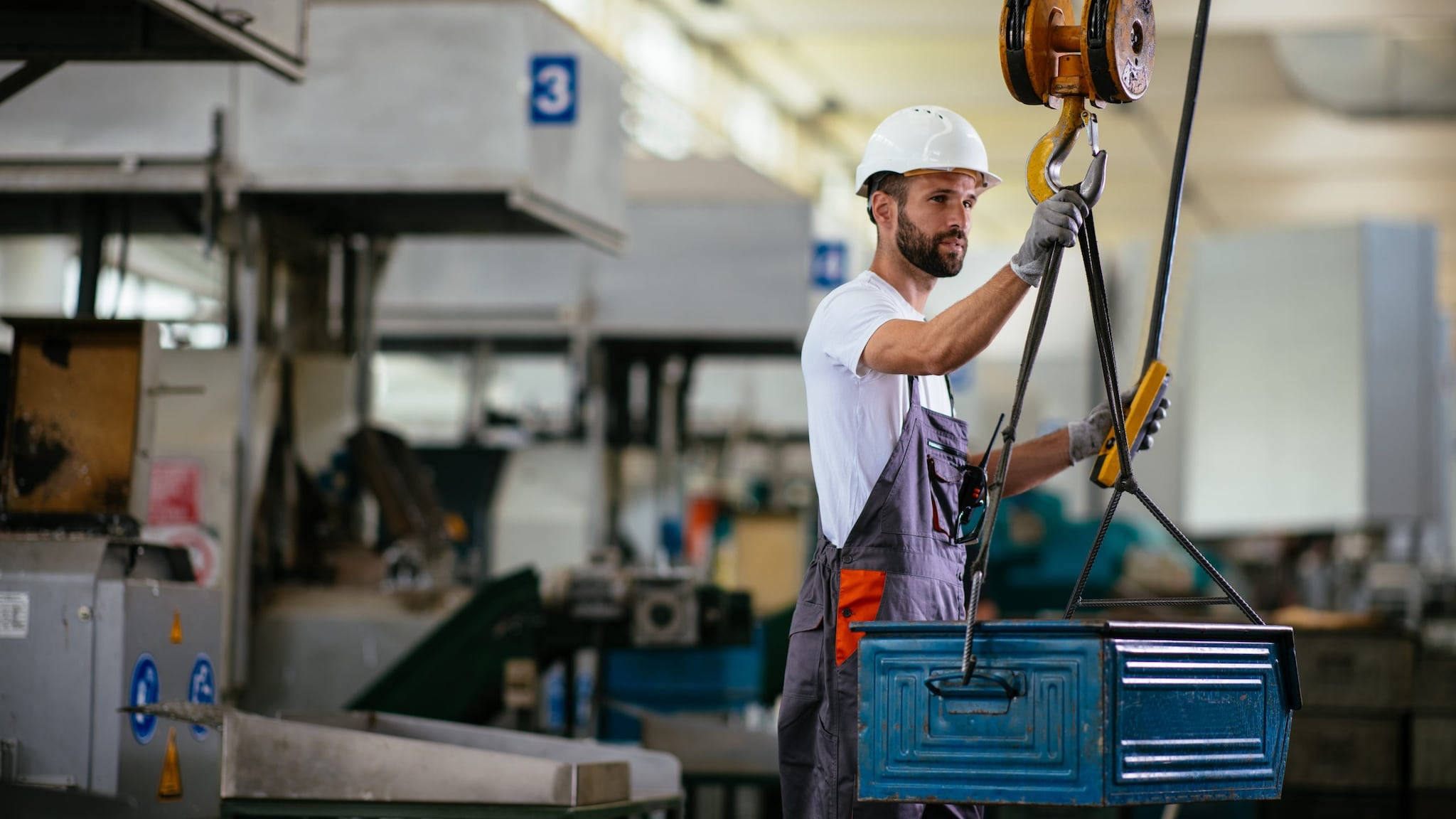 A man uses a crane to assist a lift in a manufacturing setting