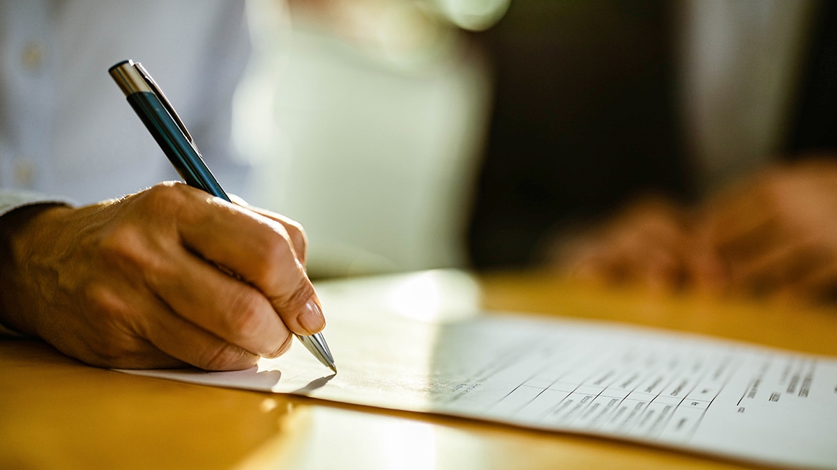 a hand holding a pen writing on a white piece of paper on top of a wooden tabletop