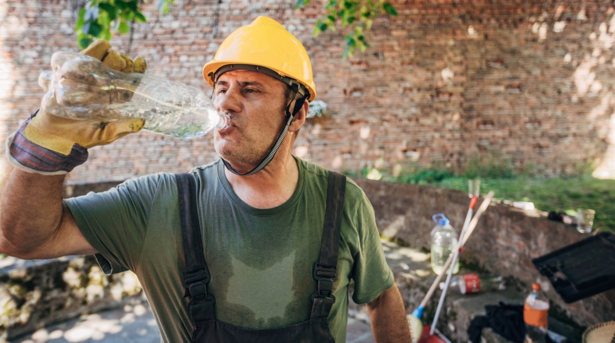 Un trabajador al aire libre sudando y tomando agua.