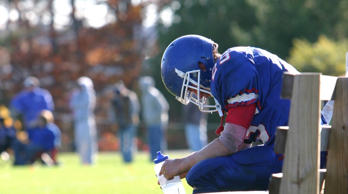 Football player resting on bench with head down