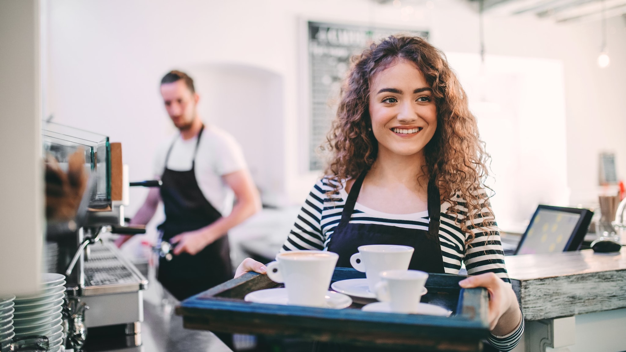 Female retail worker carrying a tray with coffee cups.