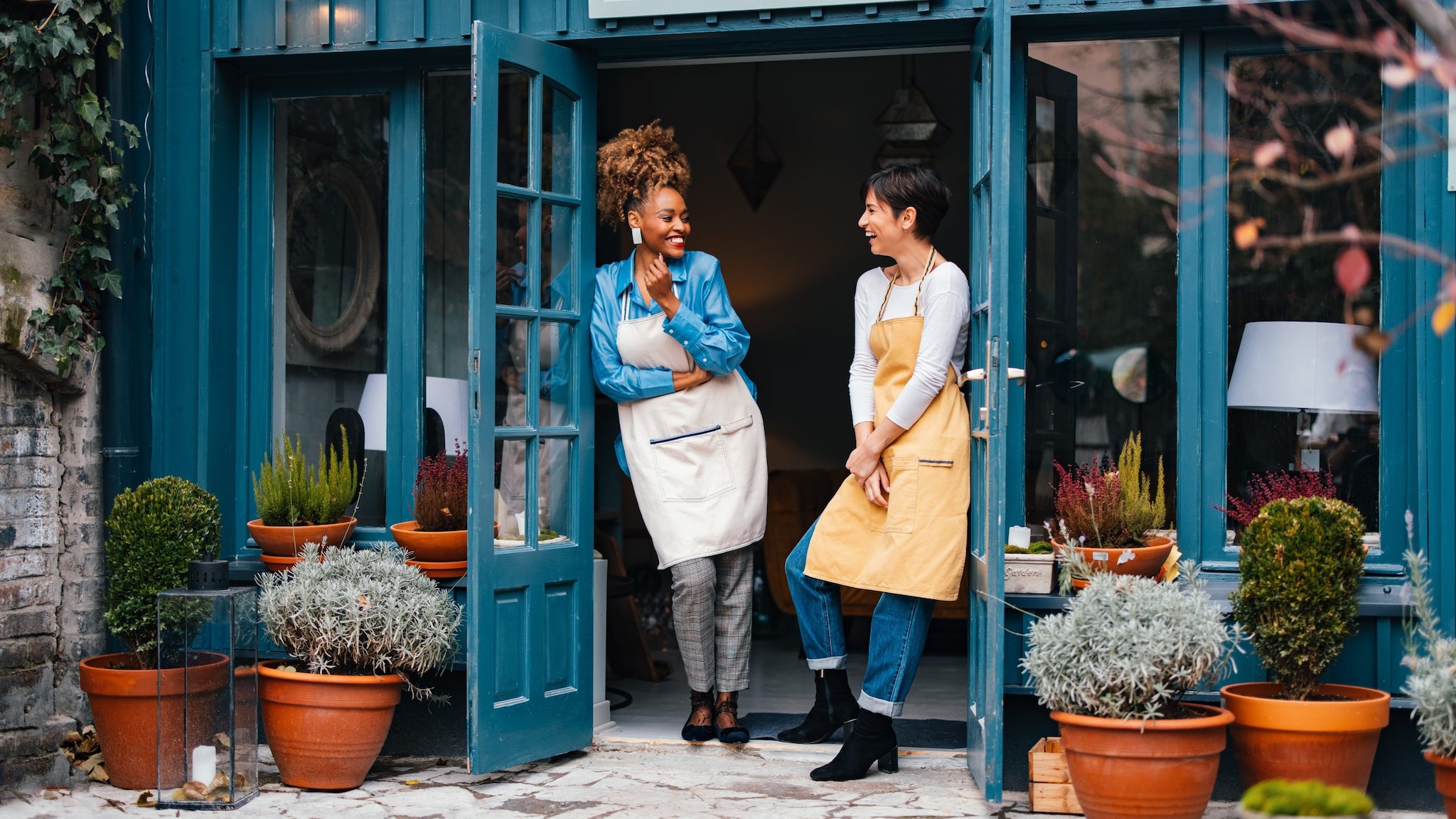 Happy African-American woman and her employee talking and laughing while standing at door of the store.