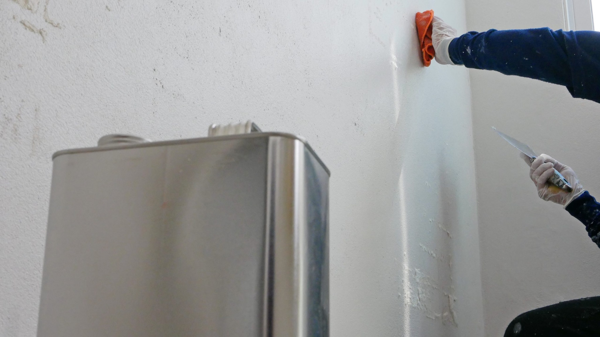 A person stripping paint off a wall with a can of paint thinner.