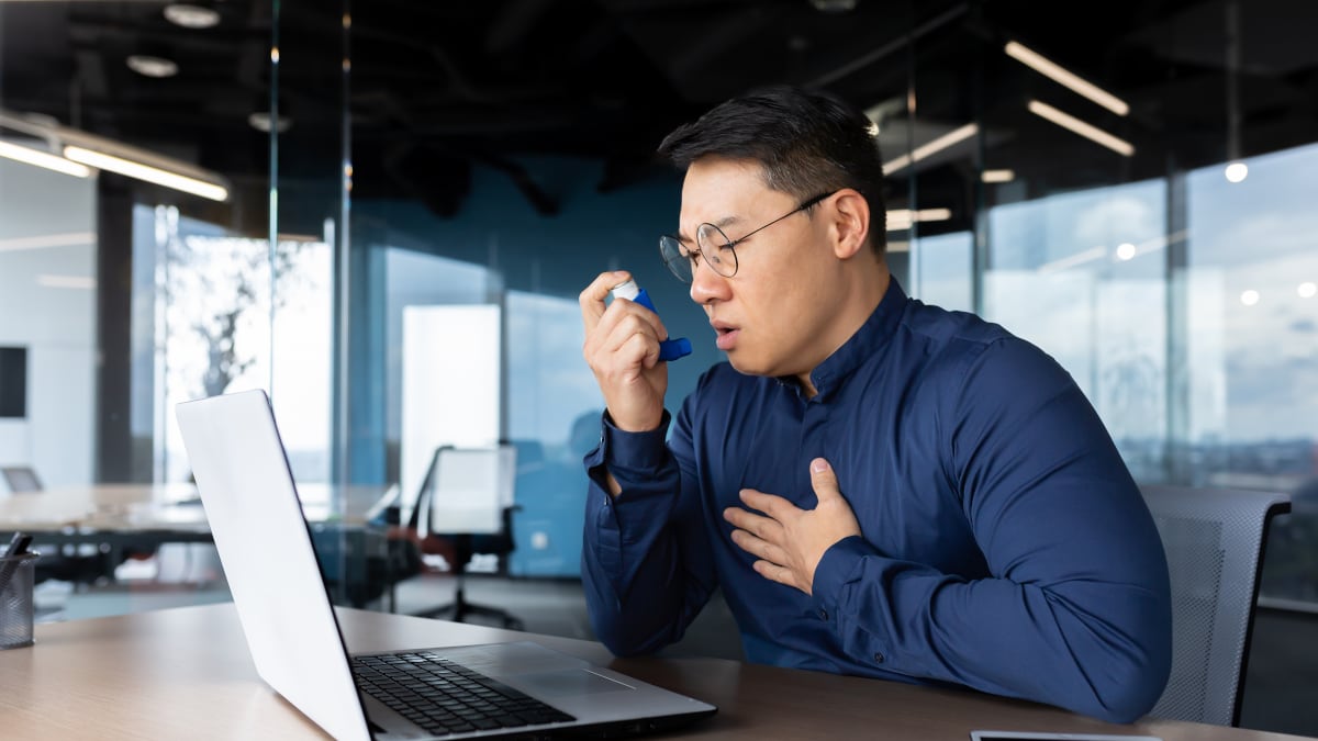 Trabajador usando un inhalador mientras trabaja con su computadora portátil.