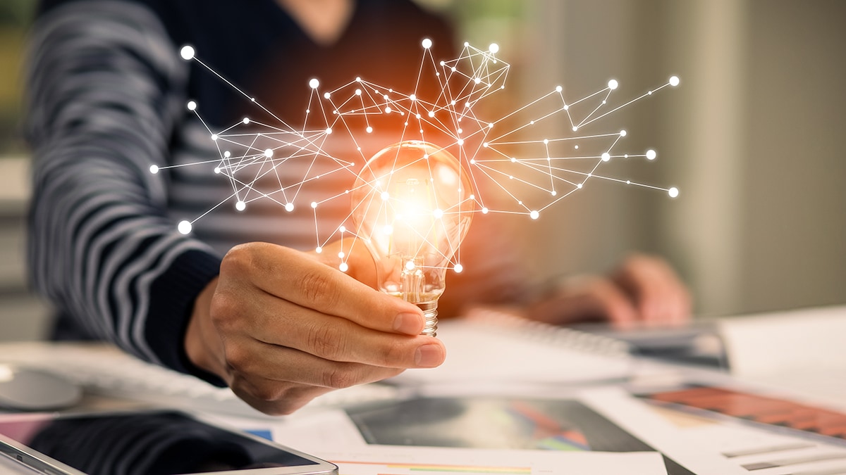 Person at desk with papers holding up lightbulb casting light