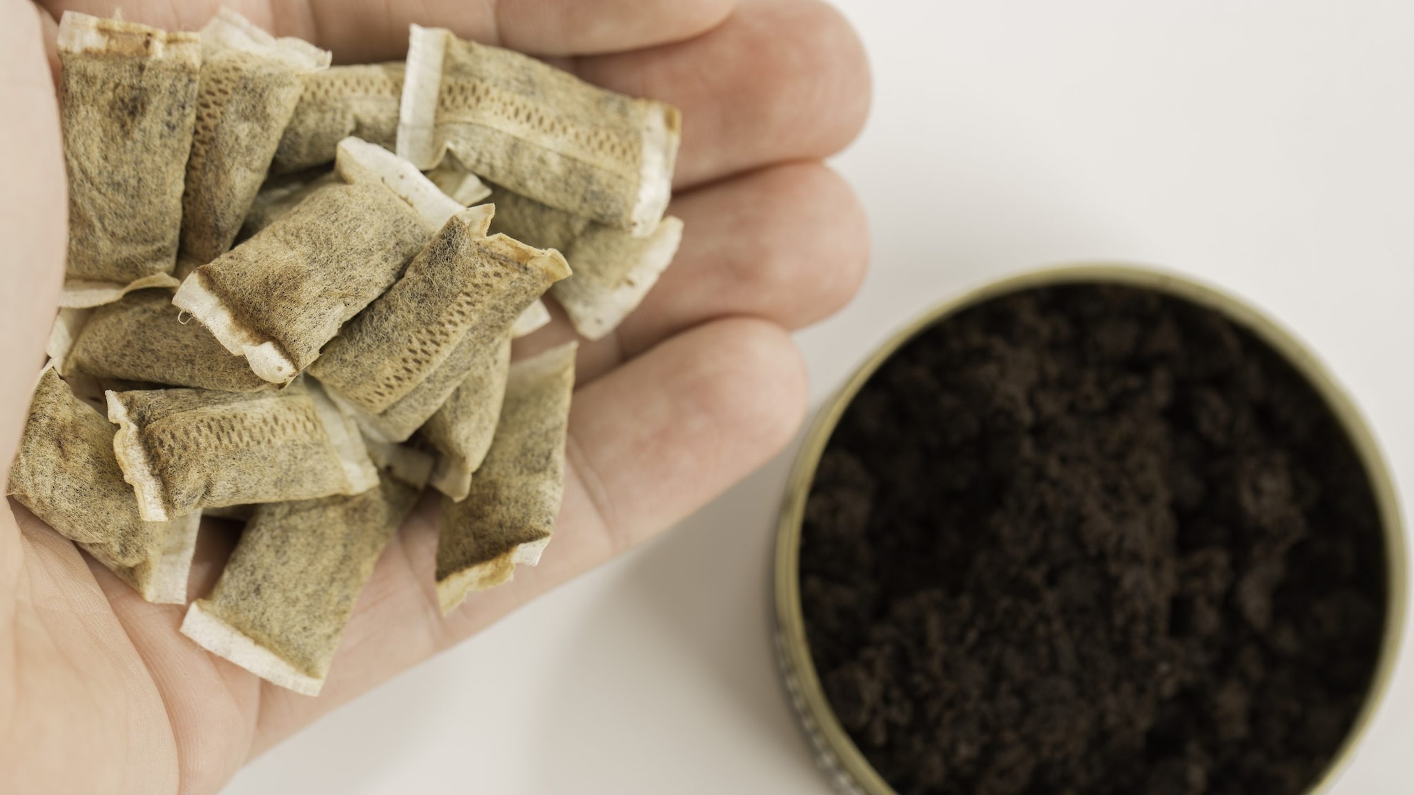 A hand holding snus with a can of snuff sitting under.