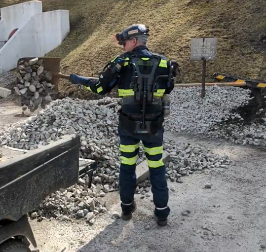 Photo of a mine worker wearing a passive, shoulder support exoskeleton while shoveling materials.