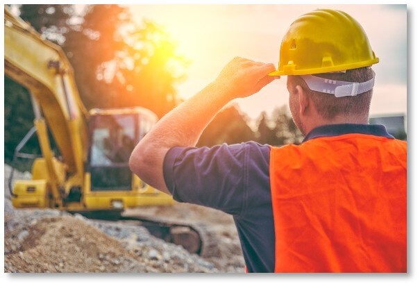 construction worker with his hand on helmet looking at field site with sun glaring