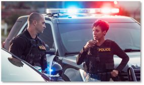 Two law enforcement officers standing next to a patrol car