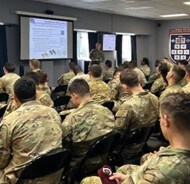 Rows of people sitting down wearing fatigues, participating in a training