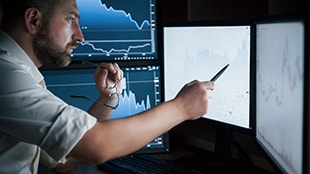 Man works in the office with multiple computer screens in index charts.