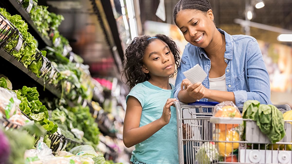 Mother and child checking a grocery list in the produce section of a grocery store.