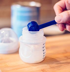 Una madre sacando leche maternizada para bebés del recipiente. Lea siempre atentamente y siga las instrucciones del envase de la fórmula para bebés.