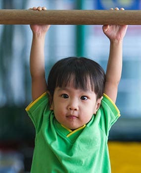 A young boy grasping a bar above his head.