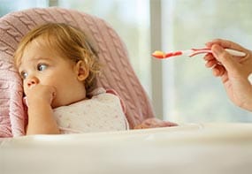 An 18-month old leaning away from her mother and the offered food.