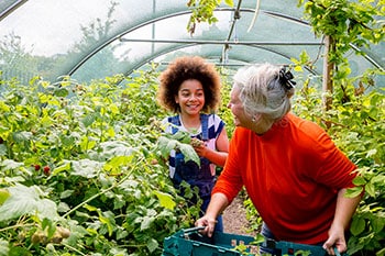 A woman and a girl interact in a garden.