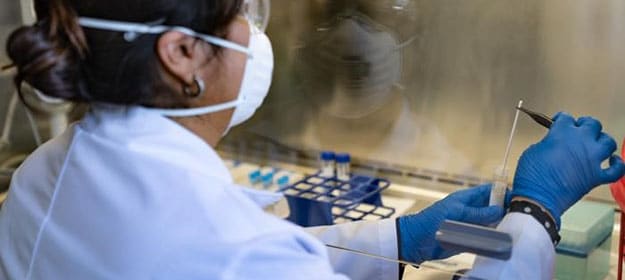 A laboratorian analyzes a participant sample under a laboratory hood in an acute febrile illness (AFI) research project.