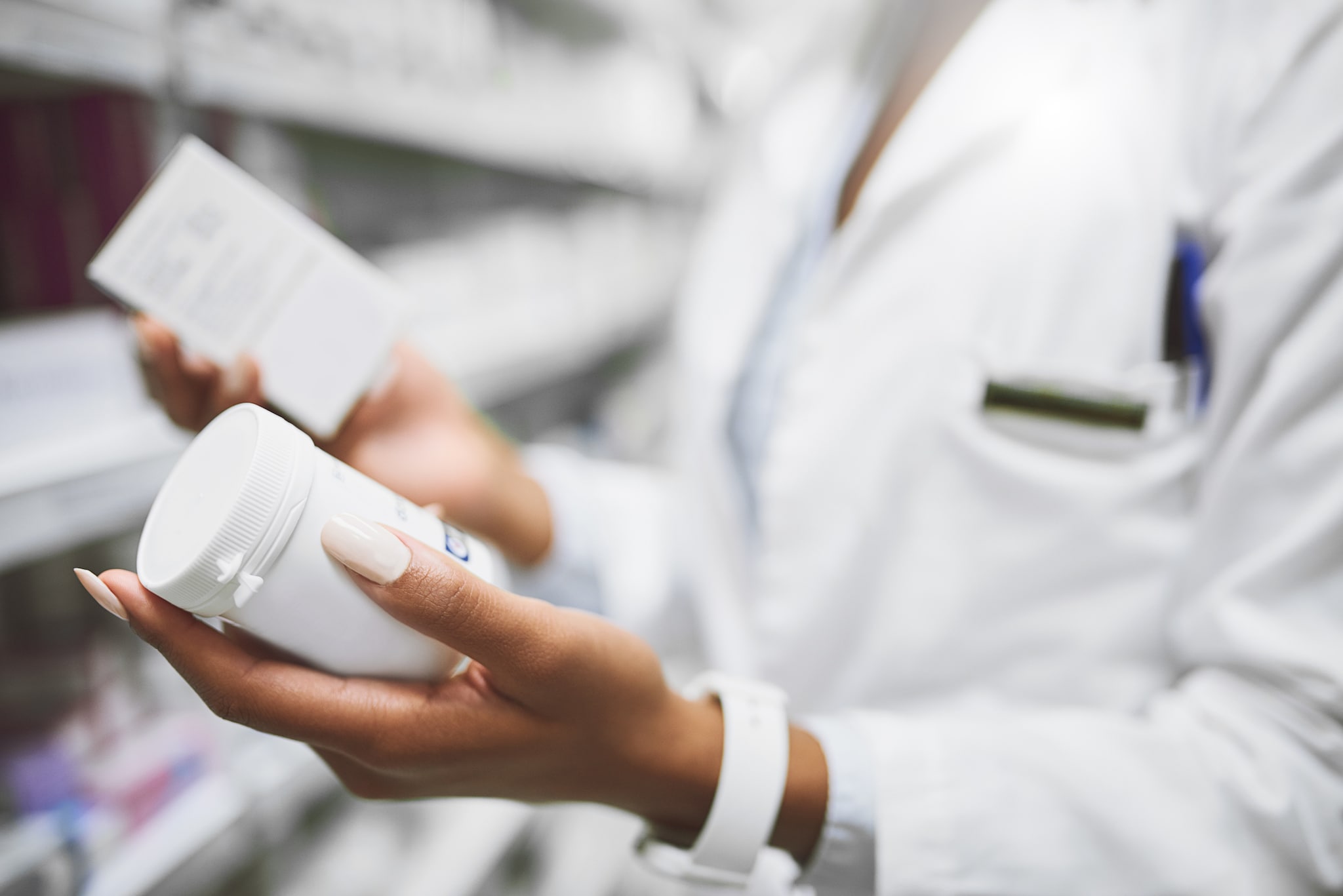 A closeup of clinician holding two prescription pill bottles in a pharmacy aisle.