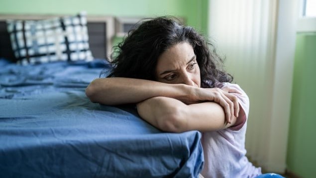 Woman with her head on the corner of a bed.