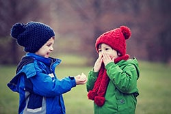 Young boy sneezing next to friend.