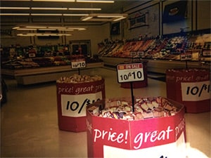 Photo of a grocery store in which unhealthy foods being actively promoted in the foreground with produce not being promoted in the background