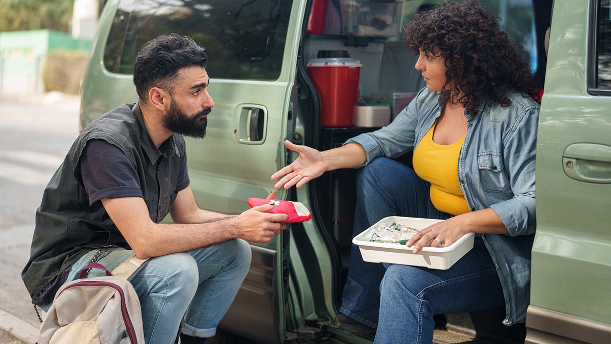 A man sits by a van to receive aid from a mobile syringe services program provider.