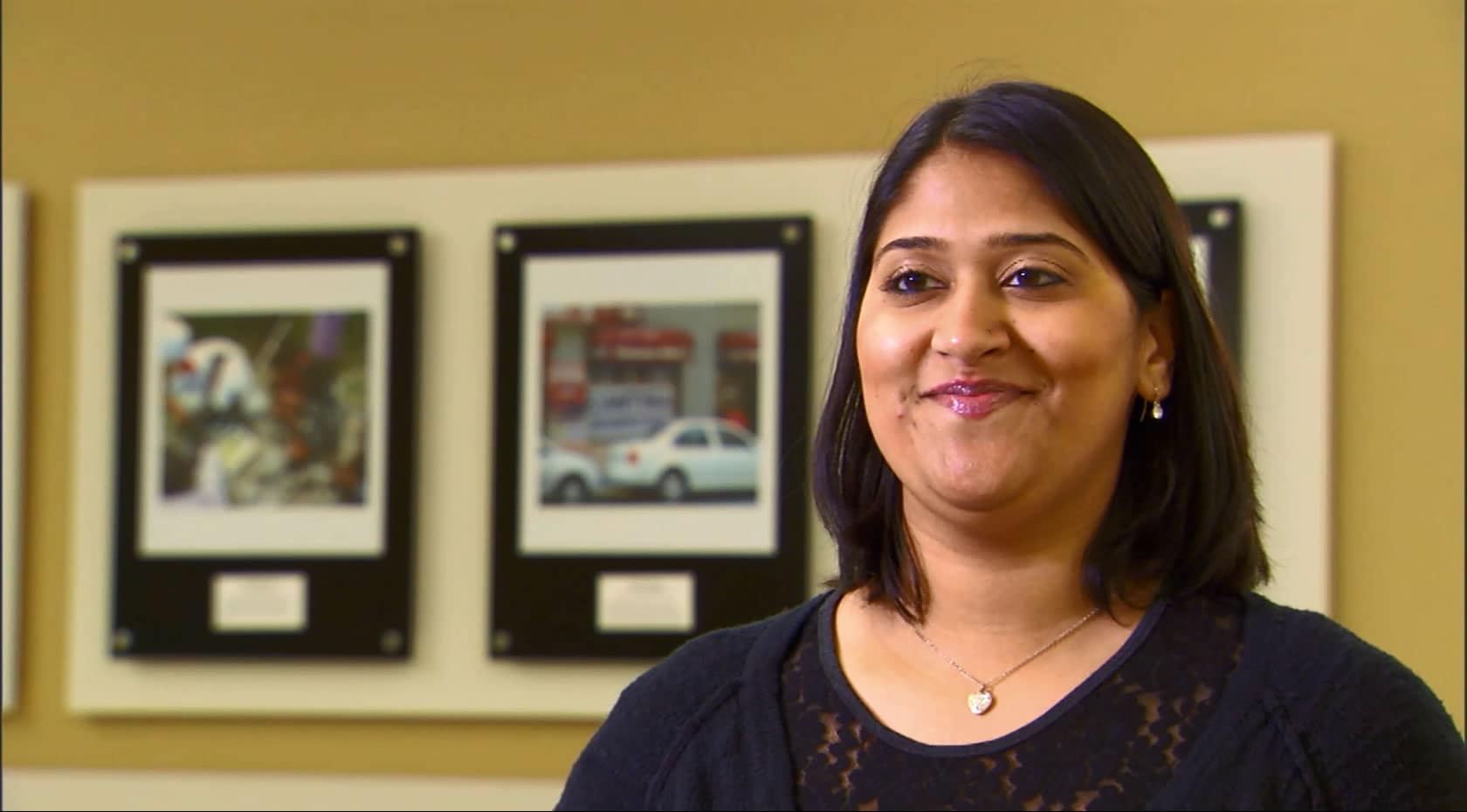 A woman smiling in front of a wall of pictures, with a look of joyful memories.