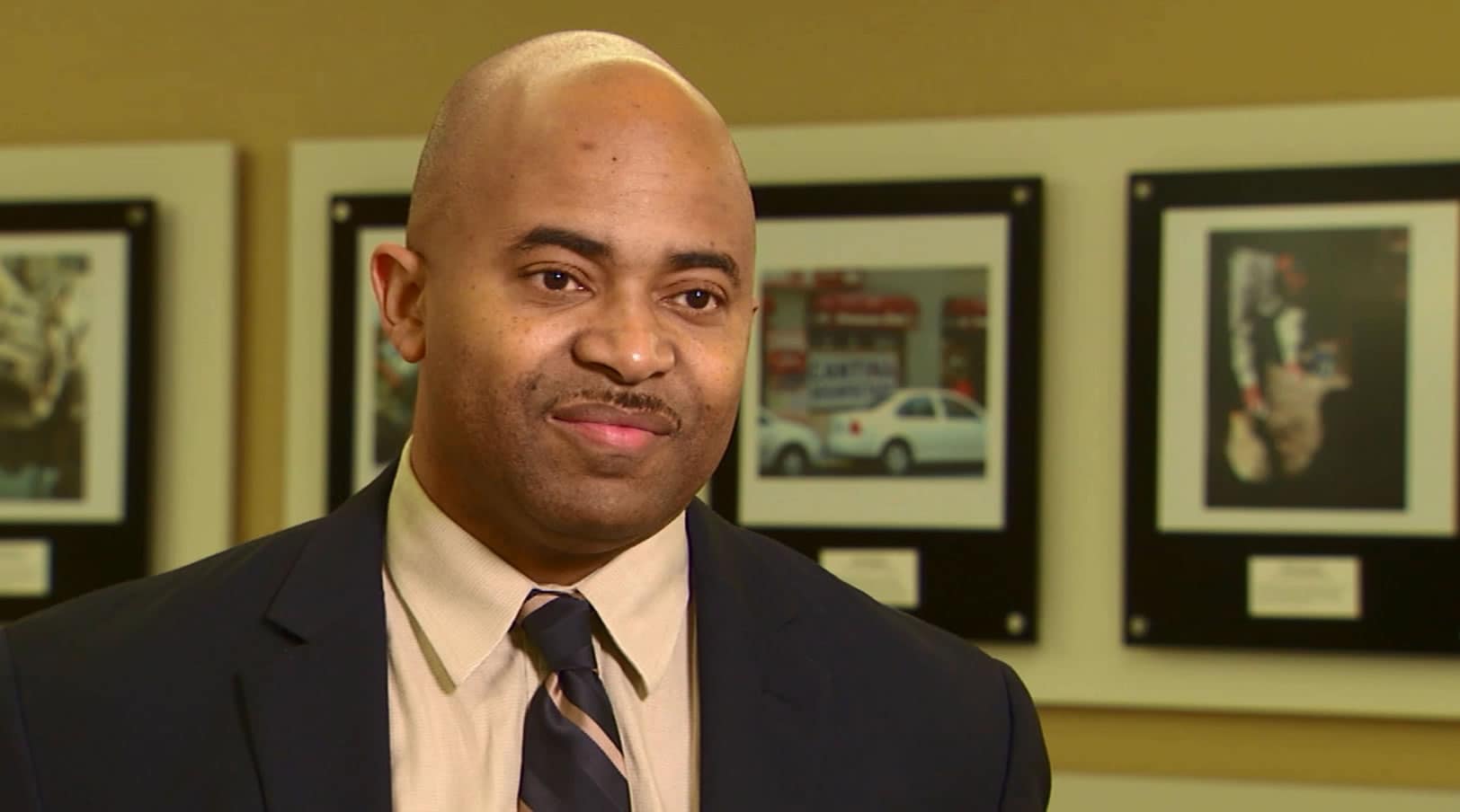 A professional man in a suit and tie standing in front of various pictures.