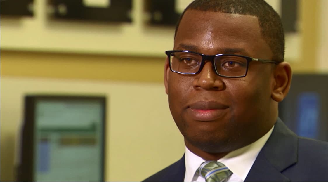 A professional man in glasses wearing a suit and tie confidently gazes at the camera.